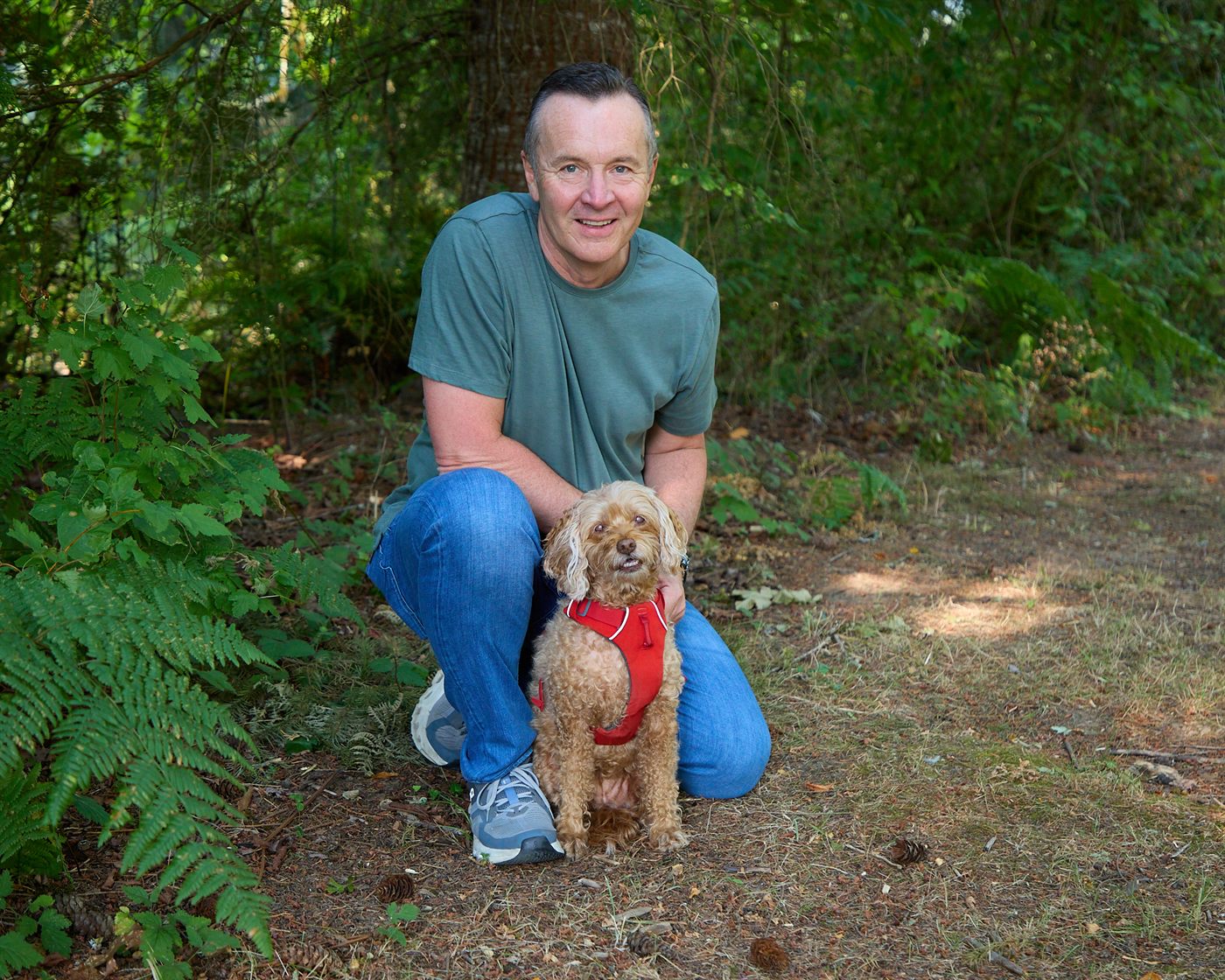 Neil Tunmore kneeling on a wooded trail beside his dog