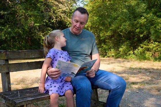 Neil Tunmore reading a picture book with his granddaughter Lana on a park bench