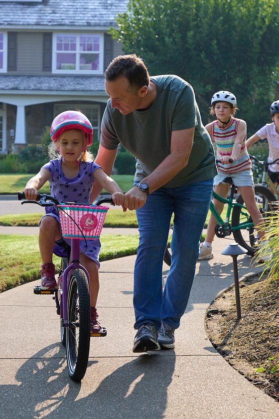 Neil Tunmore steadying a young girl on her bike along a Lake Oswego sidewalk, with two older children riding behind
